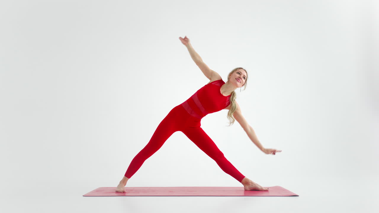 Millennial woman stretching in yoga pose meditation isolated on white background in red Sportswear. Portrait of young female yoga practitioner posing for copy space. 4k
