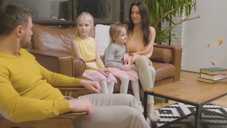 happy parents talking and spending time with their little two girls while sitting on sofa at home