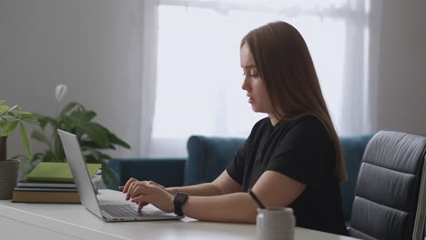 female office worker is working from home typing and sending messages by laptop translator or copyrighter freenlance work portrait of woman in room at daytime