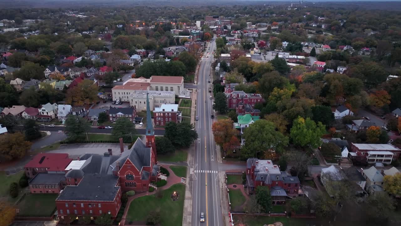 Main Street of small American town with large historic houses at dusk. Colored trees in autumn season. Aerial top down wide shot. Cathedral in downtown.