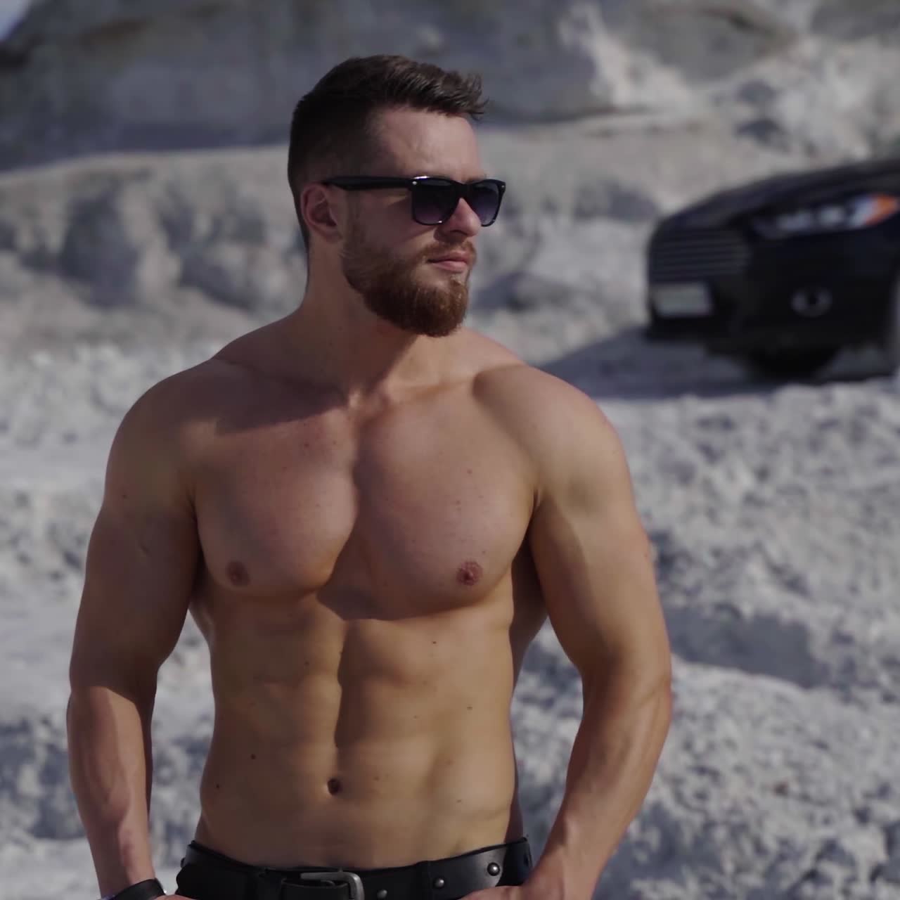 Muscular man on black car background. Strong man without shirt walking on white canyon in at sunlight. Portrait of handsome athlete outdoors.