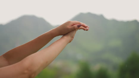 Elegant-woman-massages-hands-against-mountains-silhouette