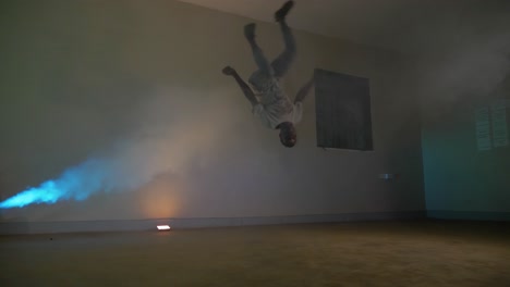 slow motion shot of a young african man in a beanie break dancing doing a windmill to jumping on his hands in colorful disco lights and smoke