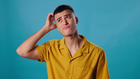 man in yellow shirt scratching his head, looking confused and thinking