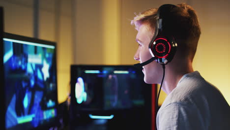 teenage boy wearing headset gaming at home using dual computer screens