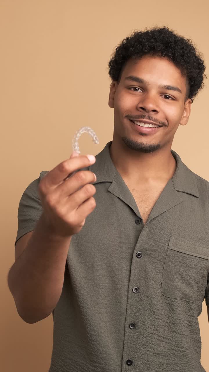 Happy young man showing invisible braces in beige studio