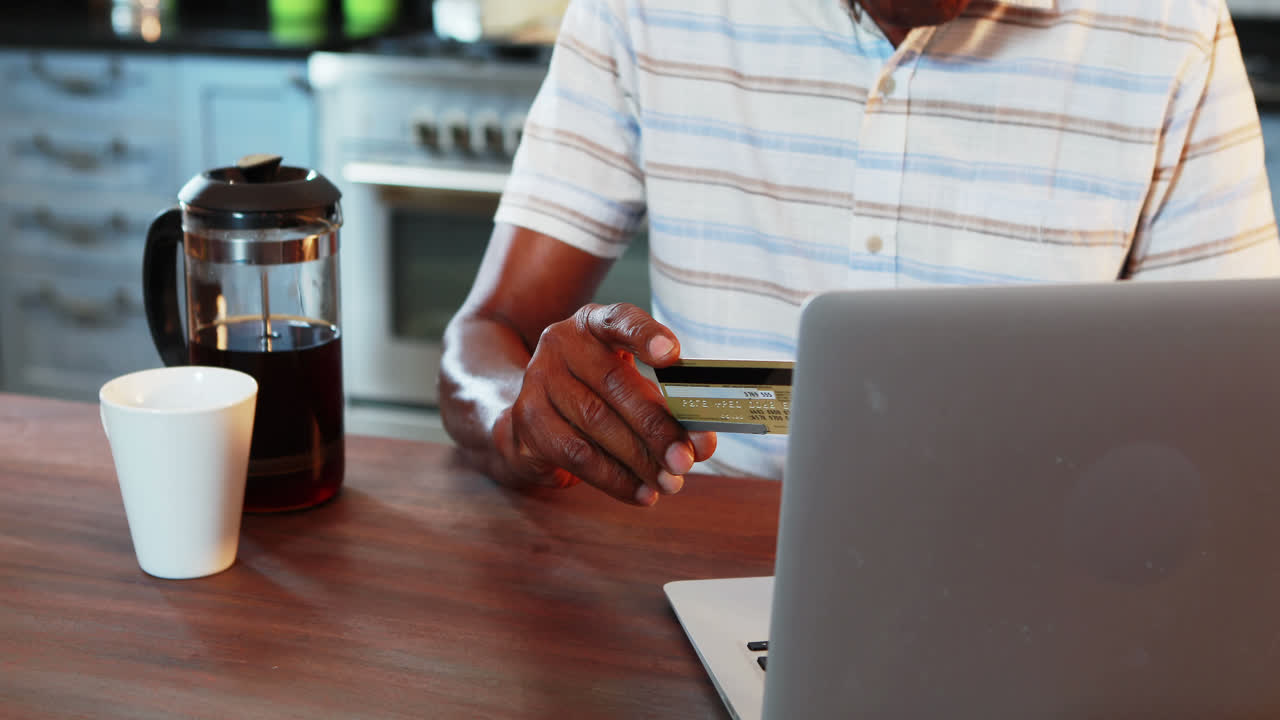 Senior man doing online shopping on laptop in kitchen at home