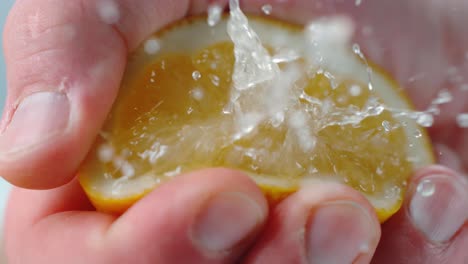 person squeezing lemon half with juice droplets in air