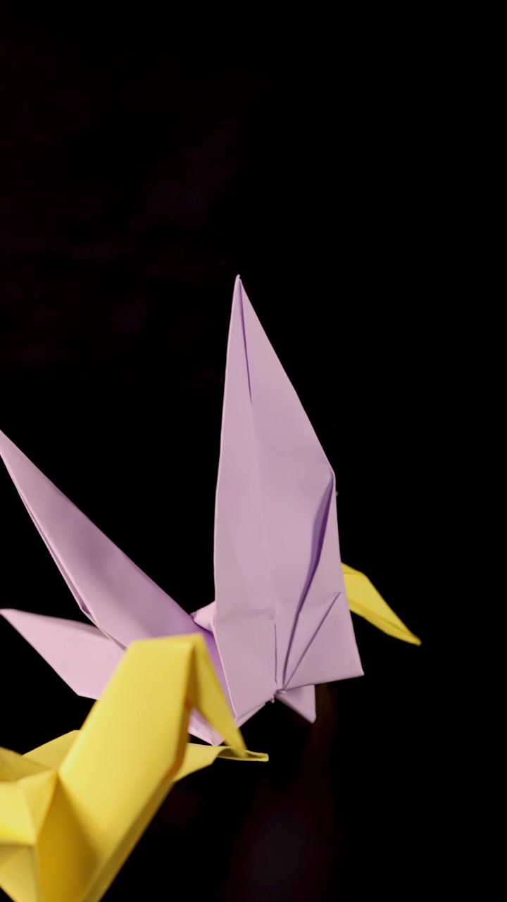Gul origamifugl taber blå stjerne, forvandles til lyserød trane på sort baggrund, studiebelysning