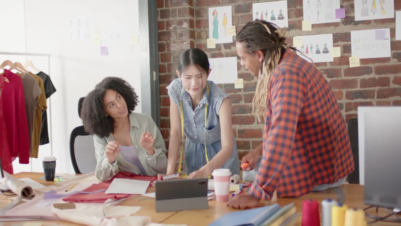 행복한 다양한 디자이너들이 노트북을 사용하고 슬로우 모션으로 패션 디자인 스튜디오에서 일을 논의하고 있습니다.