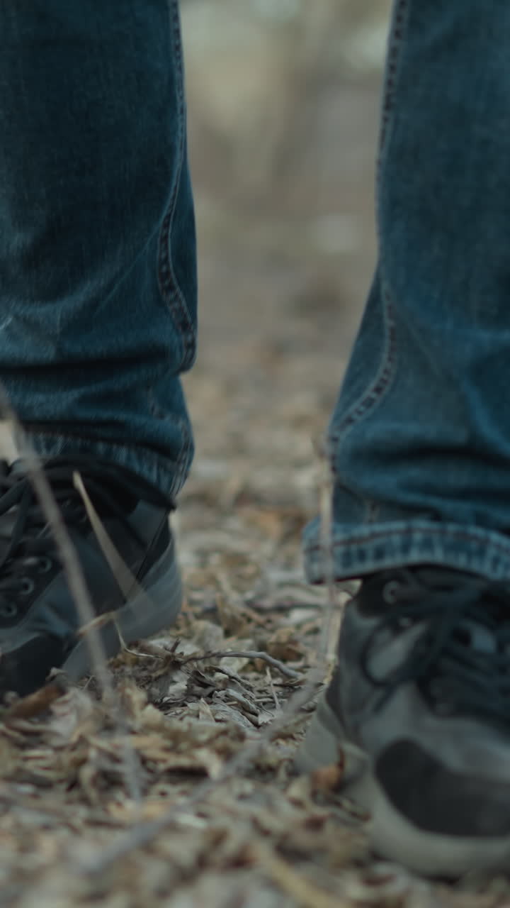 toma de primer plano de una persona caminando por un sendero del bosque, con zapatillas negras y vaqueros azules, el suelo está cubierto de hojas y ramas