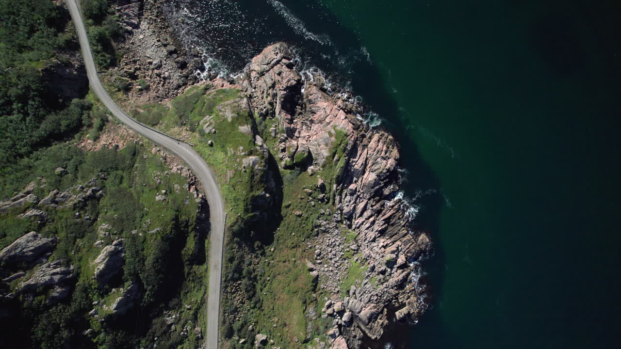 Luftfoto ovenfra af en smal, farlig norsk vej langs kystlinjen på en solrig dag