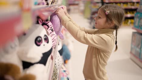 The girl is standing in a children&#039;s toy store in front the shelf and take a soft toy