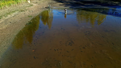 two men digging in a shallow pond with shovels to assess water levels and pond condition
