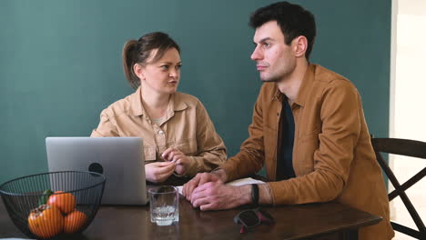 smiling woman with laptop computer and a blind man with braille book talking while sitting at table at home