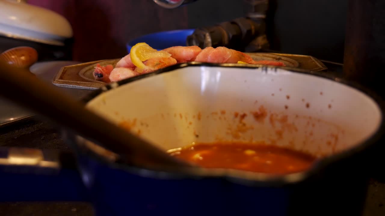 toma de mano con enfoque en rack desde una olla azul con salsa cajún a la barbacoa hasta algunos camarones congelados con limones en un tazón de plata en una antigua cocina de campo