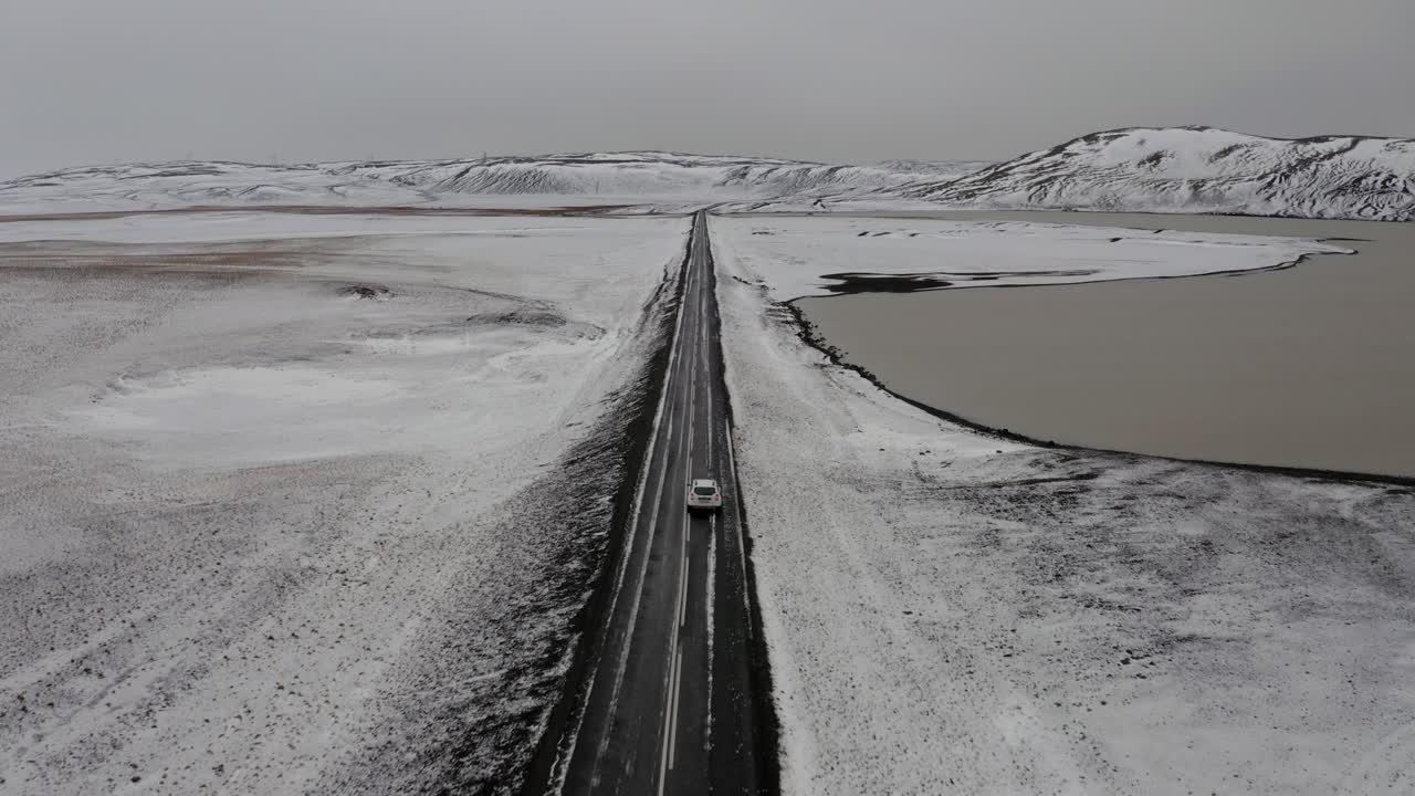 с воздуха: за машиной, едущей по заснеженной дороге возле замерзшего озера