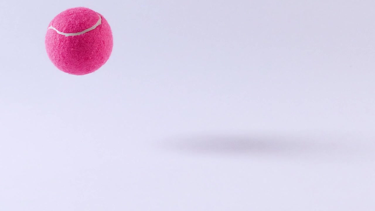 A bright pink tennis ball bounces and rolls across a minimalist white studio background