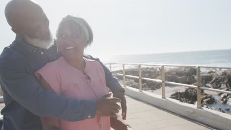 Happy-senior-african-american-couple-embracing-on-promenade-by-the-sea,-slow-motion