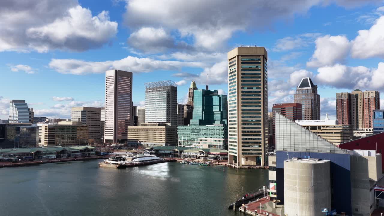 Baltimore Inner Harbor med moderna skyskrapor, vattenfrontsarkitektur, lugnt vatten och klarblå himmel. Stadssilhuett och urbant hamndistrikt på en solig dag. Bred flygbild i stigande vinkel