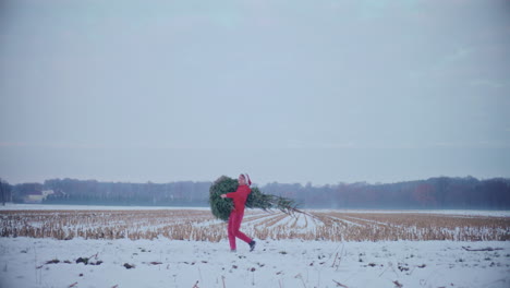 Fröhlicher-Mann-Trägt-Weihnachtsbaum-Auf-Schneebedeckter-Landschaft