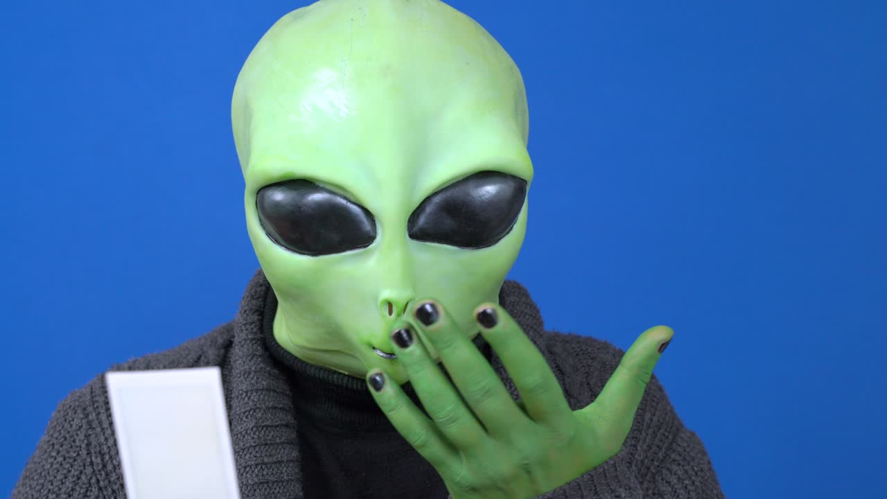 쾌적한 뜨개질 재을 입은 휴머노이드가 사진, 포스트카드 또는 노트를 읽고, 파란색 배경, 아픈 외계인이 재채기 또는 기침, 공상 과학 영화 또는 극장 제작에 출연하는 배우