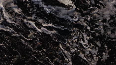 foamy waves crash over black pebbles and melting ice on iceland’s diamond beach