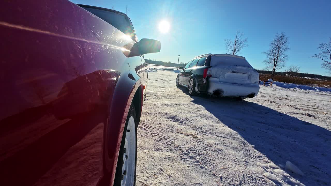 Lavt perspektiv fra forhjulet viser en bil, der drifter hen over sneen og kaster sne op bag sig i solskinnet.