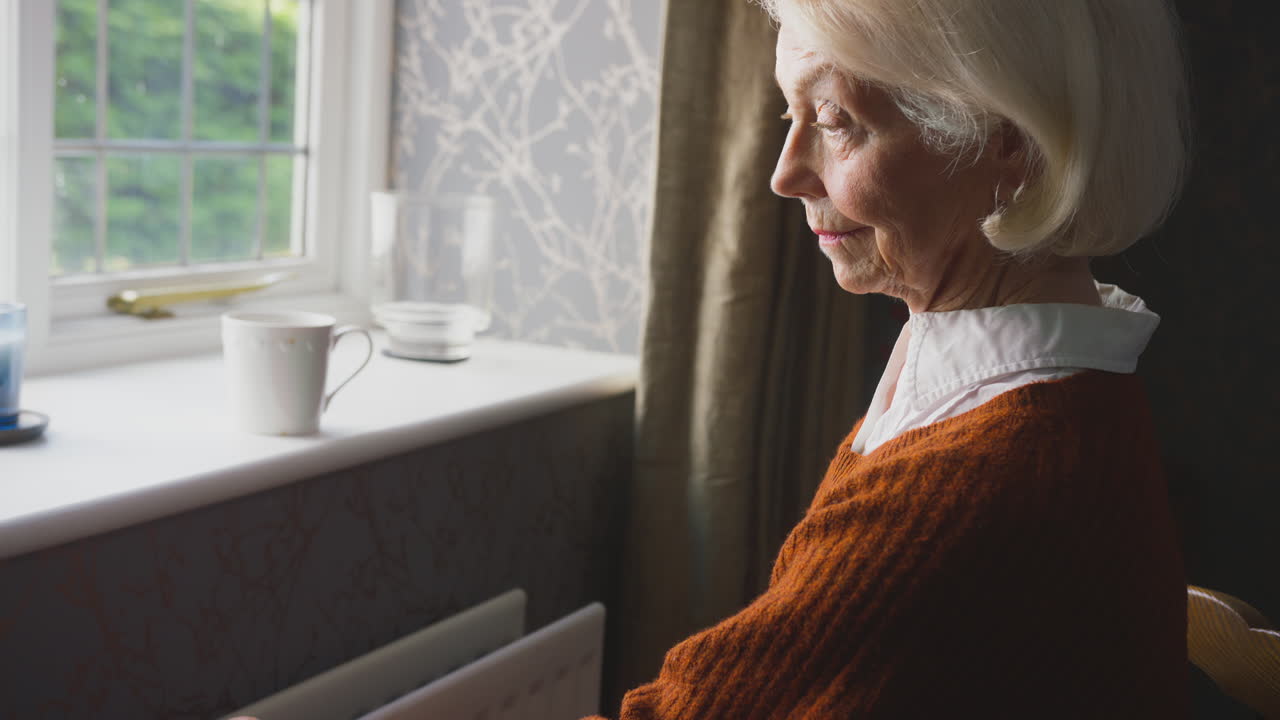 Senior Couple Sitting By Radiator At Home With Man Putting Reassuring Hand On Woman's Shoulder