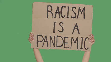 racism is a pandemic. protest text message on cardboard. stop racism. police violence. banner design concept. hands holding a poster a green screen, chroma key. close up. slow motion