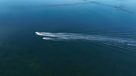 Cinematic-aerial-drone-footage-of-water-skier-following-boat-along-glassy-Fornells-Bay-in-Menorca,-Spain