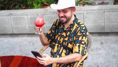 hombre hispano con cóctel navegando por el teléfono inteligente