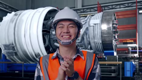 close up of asian male engineer with safety helmet smiling and clapping his hands while standing with airplane engine maintenance conducted, analytics checking the turbine
