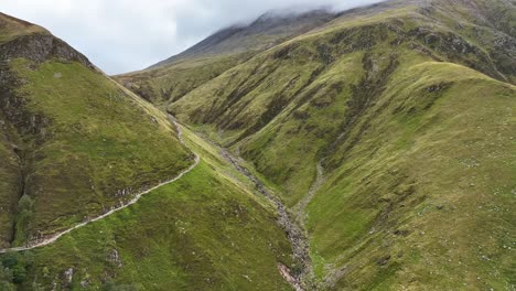 4k aerial angle revealing ben nevis in the clouds, lifting up from hikers pathway above glen nevis, fort william