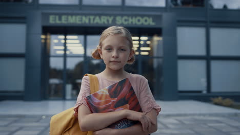 Little-school-girl-posing-at-campus-door-close-up.-Blonde-child-holding-books