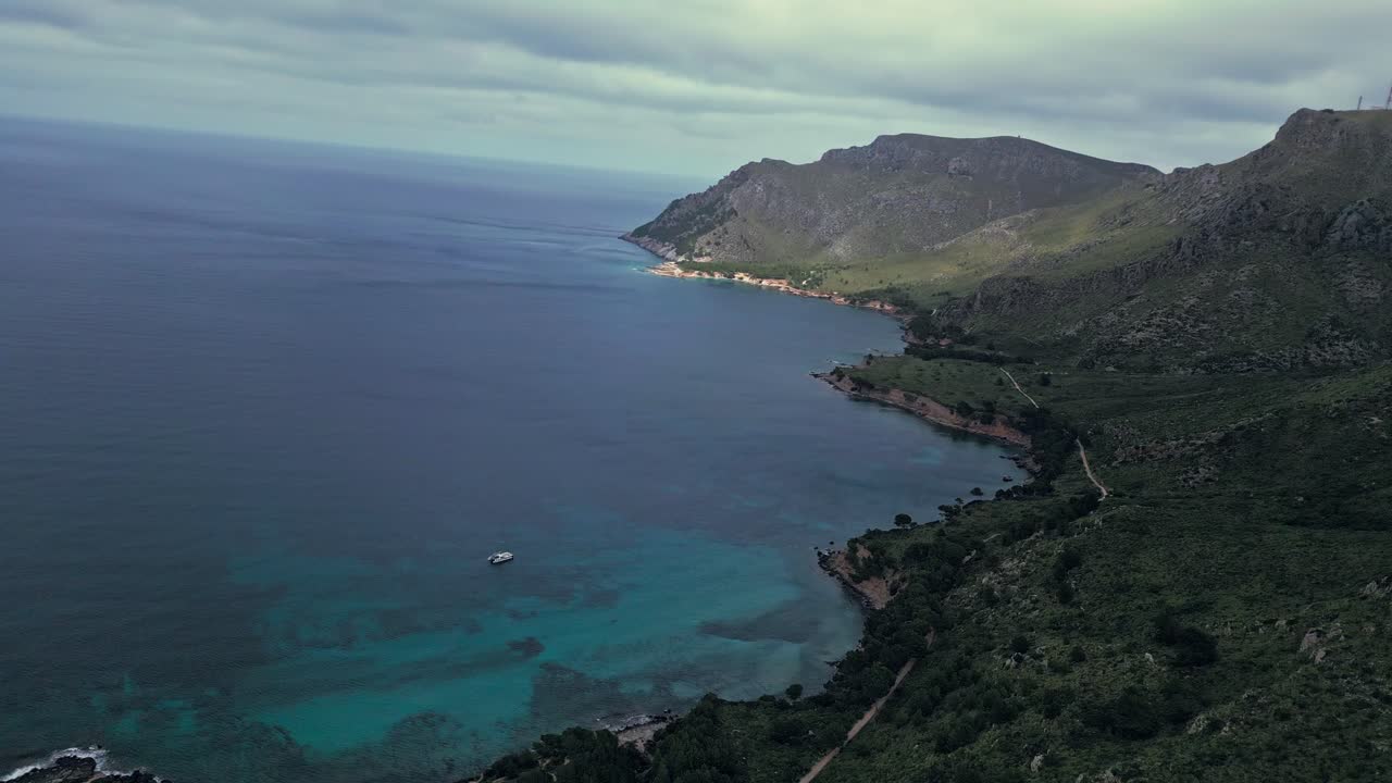 Un drone FPV riprende la costa frastagliata della Maiorca nord-orientale vicino a Betlem, mentre la luce del sole filtra tra le nuvole, illuminando il drammatico paesaggio marino