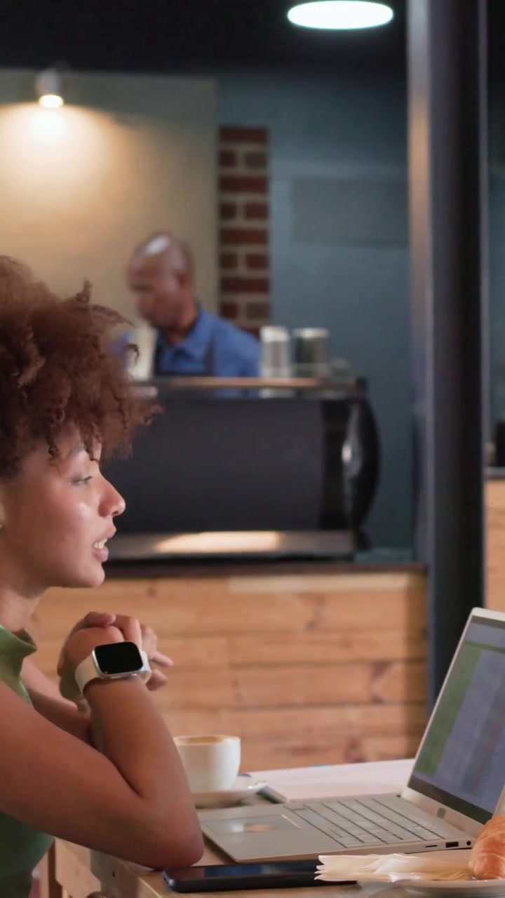 Video verticale: Donna con un top verde che entra e apre il laptop in un caffè mentre lavora con il caffè.