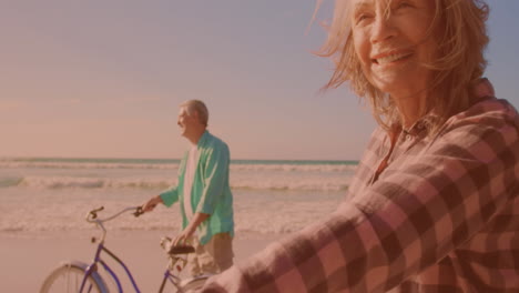 happy caucasian senior couple riding bicycles together at the beach