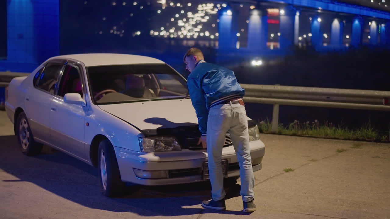 밤, 다리, 길가, 자동차, 후드 열림, 남성 운전자가 파란색 다리 조명 아래 엔진에 몸을 숙여 부품을 점검하고, 긴장된 고독, 젖은 포장 도로의 반사, 안전 난간 배경, 견인차를 기다리는 모습