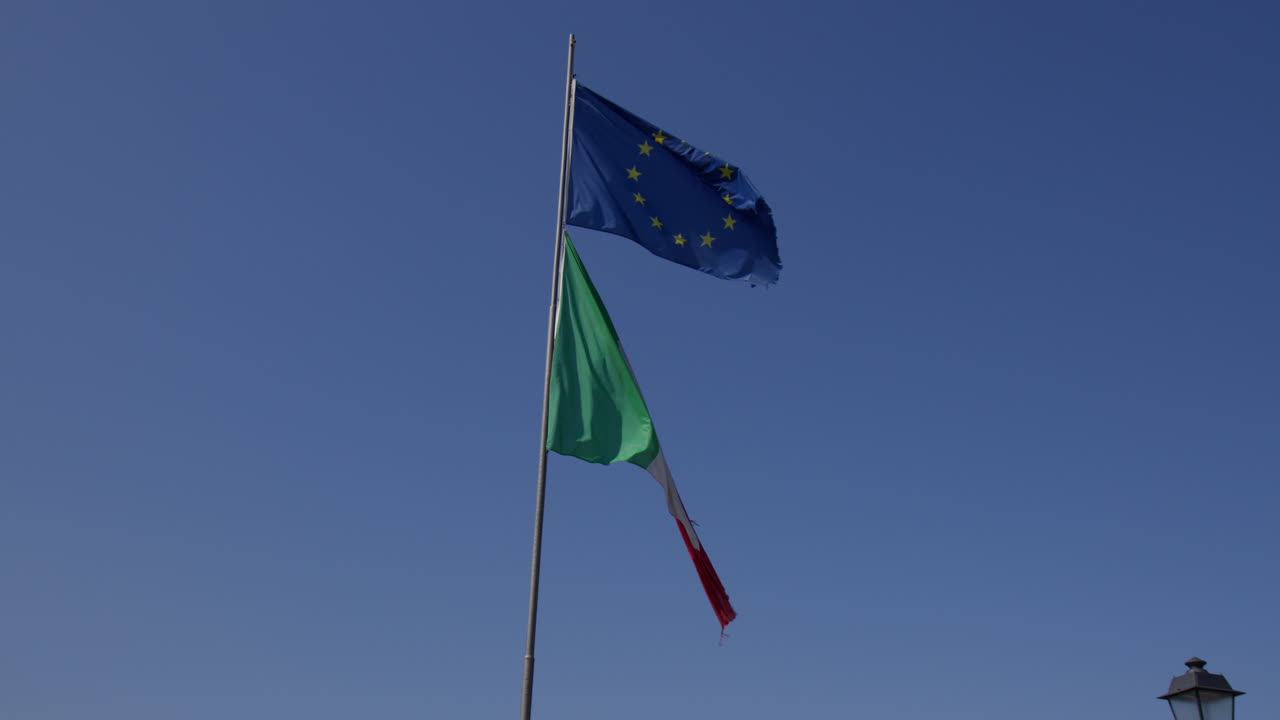 Le bandiere di Italia ed Europa che sventolano fianco a fianco contro uno sfondo di cielo blu a Bellagio, Lombardia, Italia - Inquadratura dal basso.