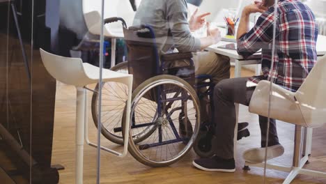 video of creative disabled man in wheelchair discussing with male colleague in modern office