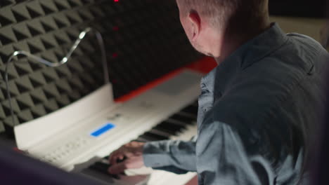 side shot of a man in a light-colored long sleeve shirt playing a white piano. set against a dark, soundproof background, focusing on the intensity and concentration of the musician as he performs