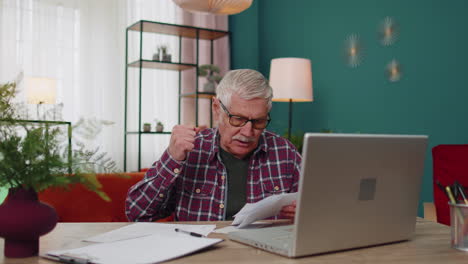 Grandfather-calculating-household-bills-bank-loan-online-domestic-expenditures-payment-on-laptop-app