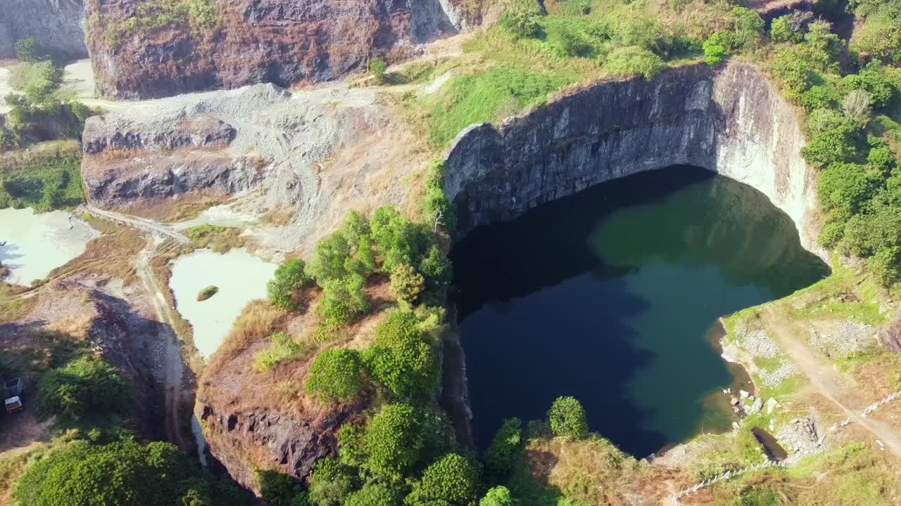 Drone view of rock quarry in India, deep pit with water, rugged cliffs, mining landscape surrounded by green trees. Shows industrial site, excavation, natural textures, perfect for geology or mining