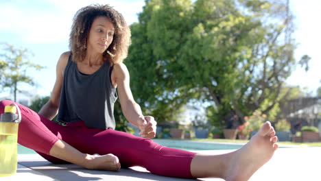 Happy-biracial-woman-practicing-yoga-sitting-by-pool-in-sunny-garden,-copy-space,-slow-motion