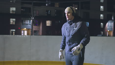 man wearing headphones and joggers lifts and traps ball on outdoor sports court at night with urban residential buildings and bright lighting in the background