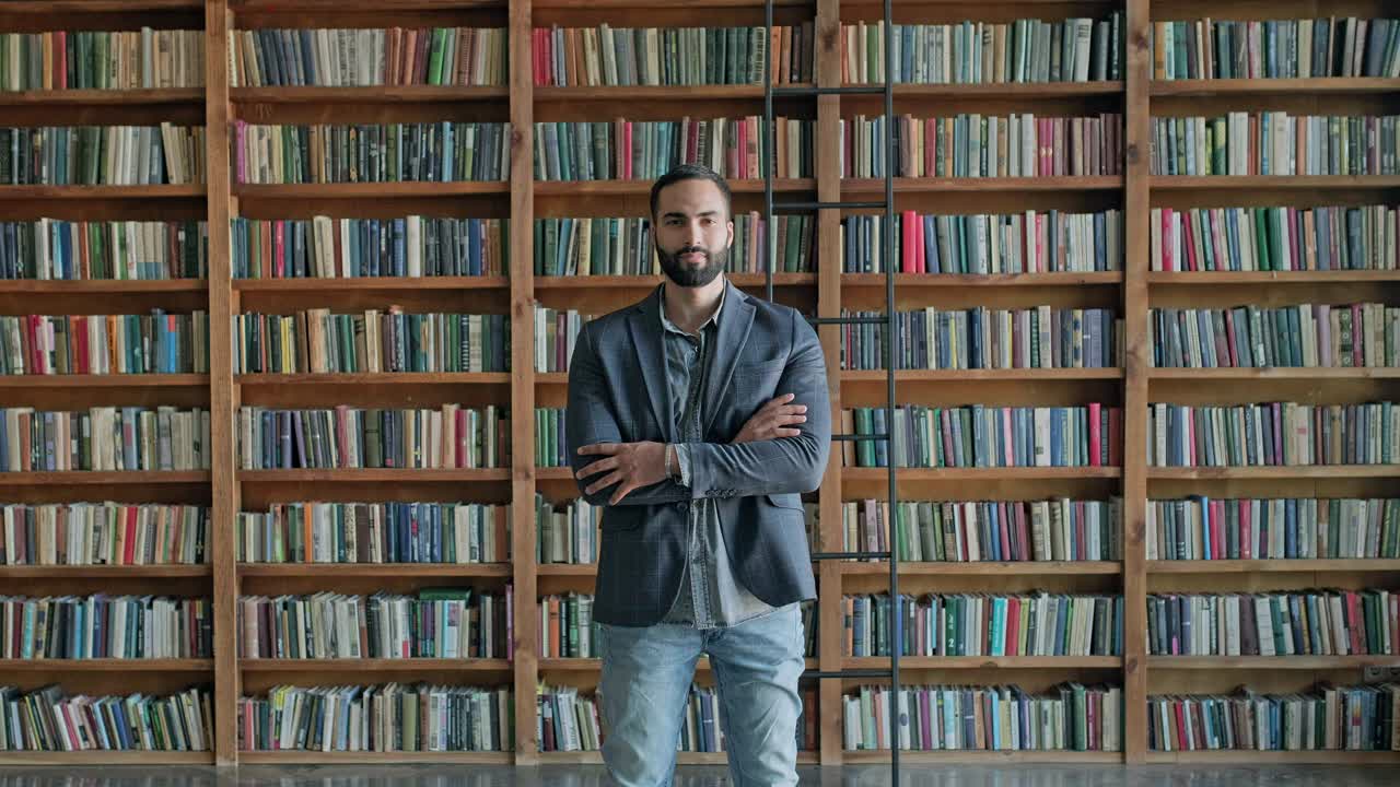 un tipo está de pie en la biblioteca. una morena atractiva con barba de oriente medio.