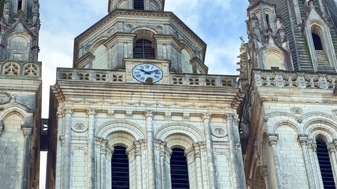 Tilt up shot from sculpted statues to cathedral clock on Saint-Maurice Cathedral facade in Angers, revealing detailed gothic architecture. France