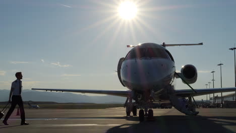 piloto con equipaje caminando hacia el avión en el aeropuerto con el sol brillante en el cielo