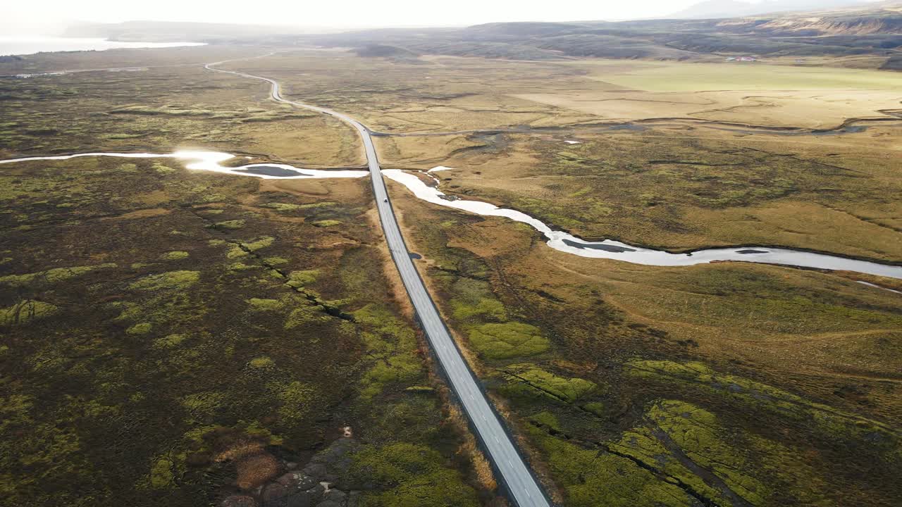 Beautiful aerial of a distant car driving over a long road running through a stunning Icelandic landscape on a sunny day